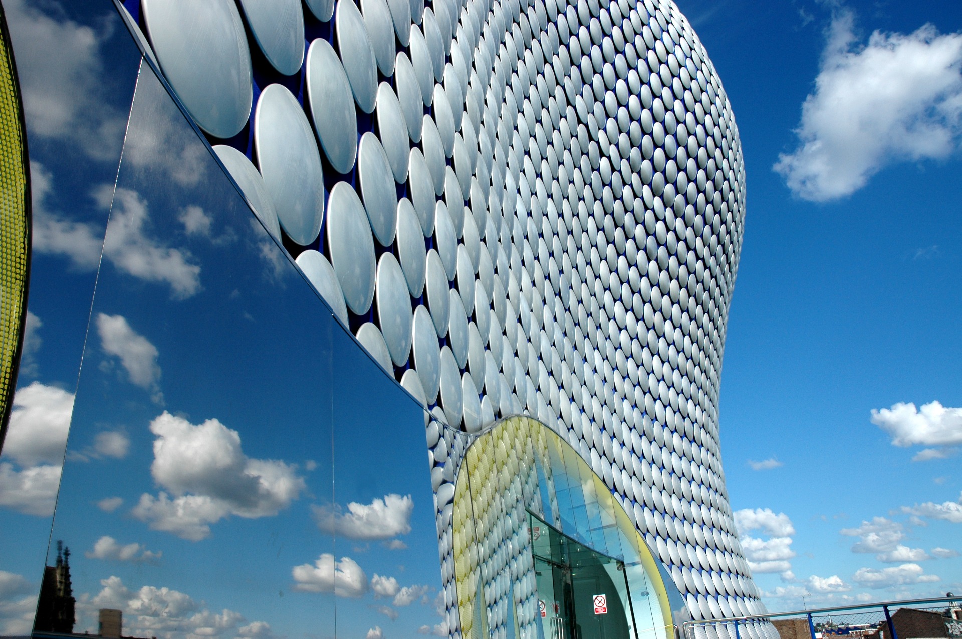 Curved building facade covered in repeating white circular panels against a bright blue sky with clouds.